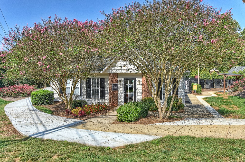 a small house with a sidewalk and trees in front of it