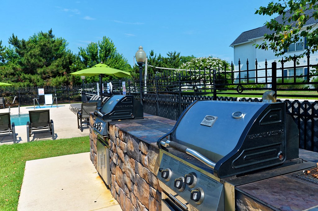 a backyard with a grill and a pool with chairs and umbrellas