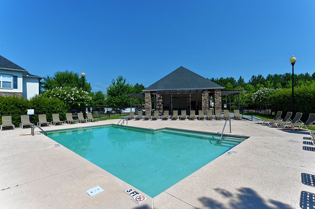 a swimming pool with chairs around it and a pool house in the background
