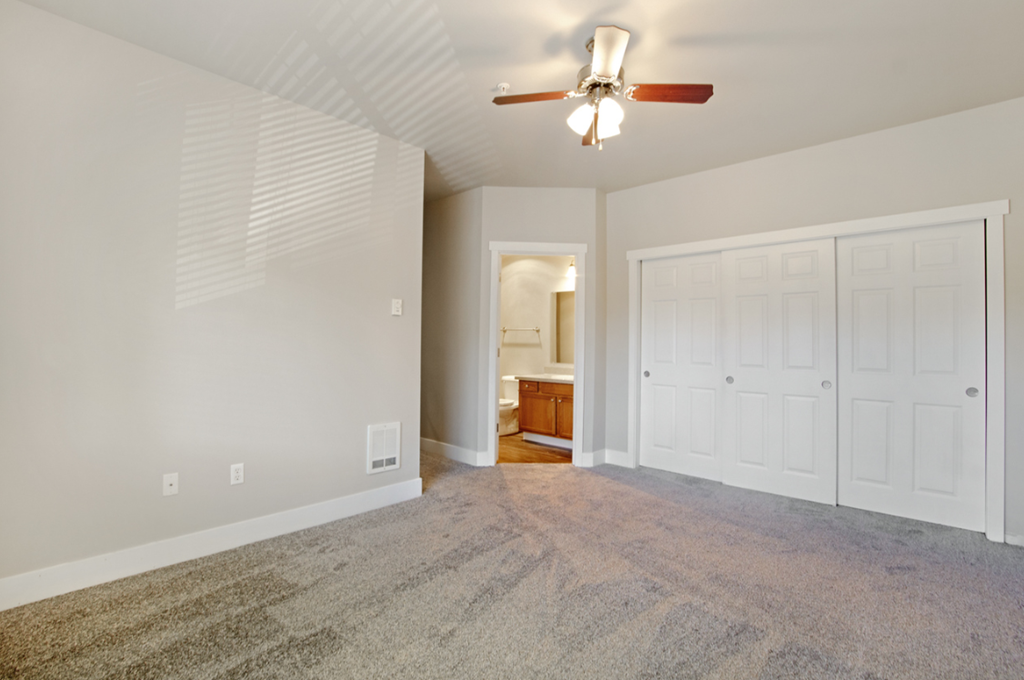 an empty living room with a ceiling fan and white doors