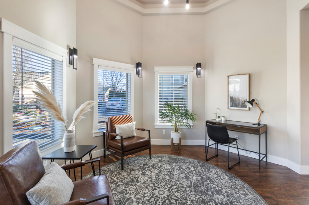 a living room with two windows and a desk with a chair