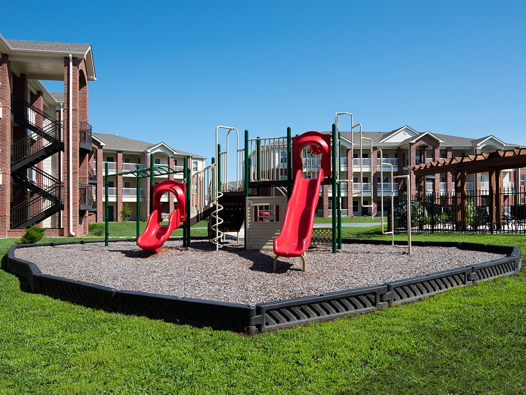 a playground with two red slides in front of an apartment building