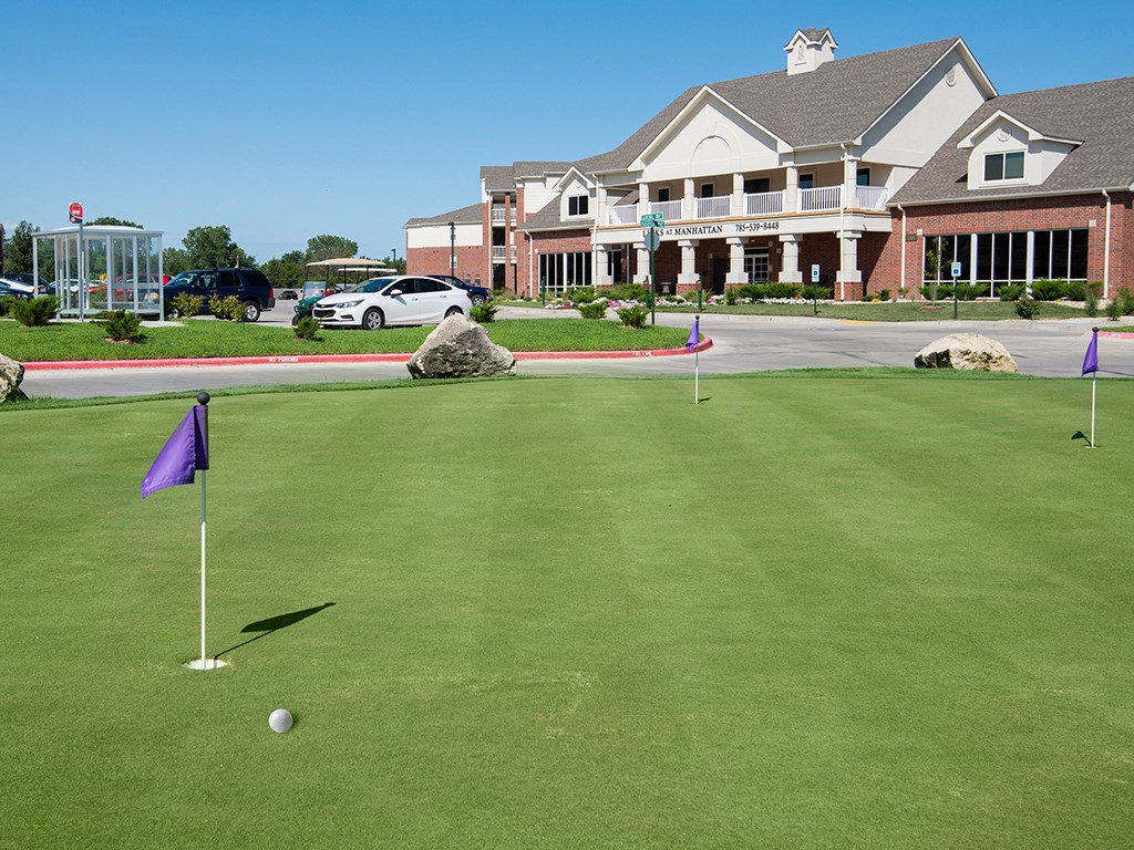 a putting green in front of a clubhouse with a golf ball on it