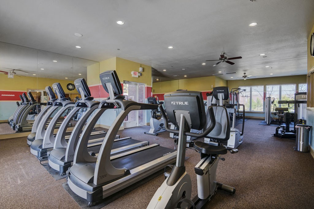 a gym with cardio equipment and a ceiling fan