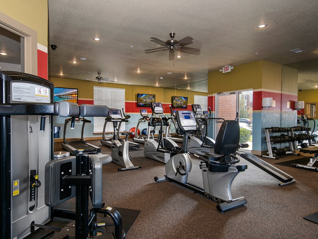 a gym with cardio machines and a ceiling fan