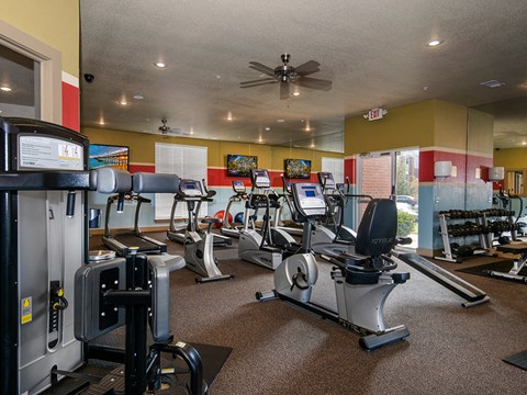 a gym with cardio machines and a ceiling fan