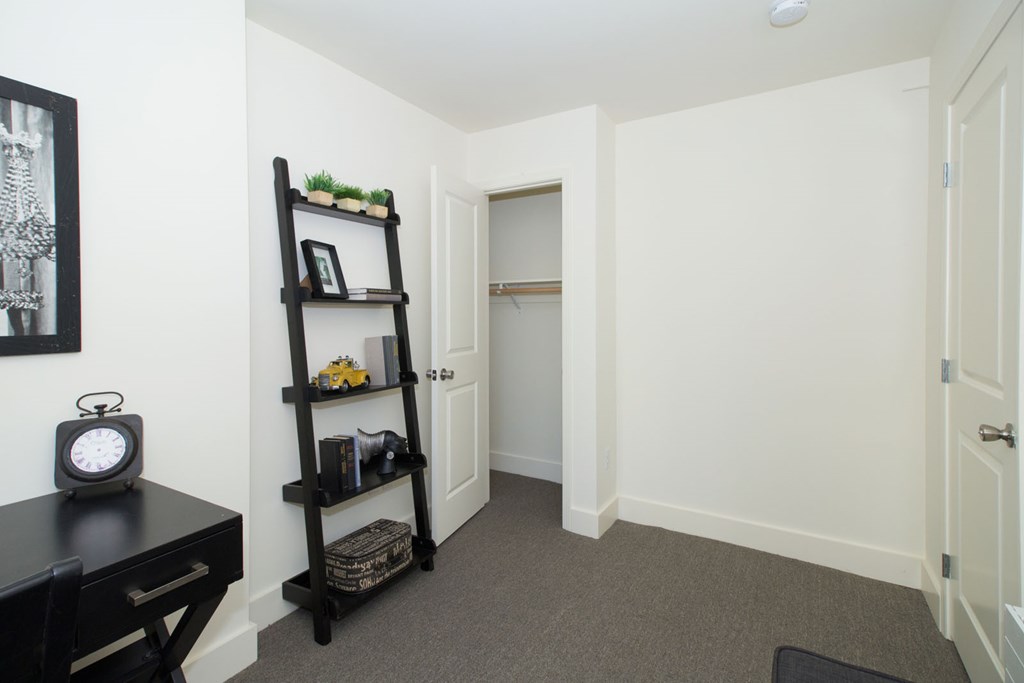 A small room with a black desk and a shelf with a clock on it.
