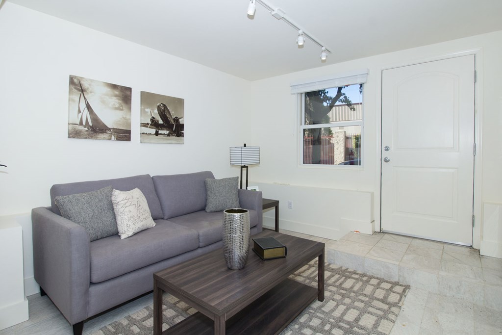 A grey couch with a grey pillow and a grey cushion is sitting in a room with a white wall and a picture of a sailboat hanging on it.