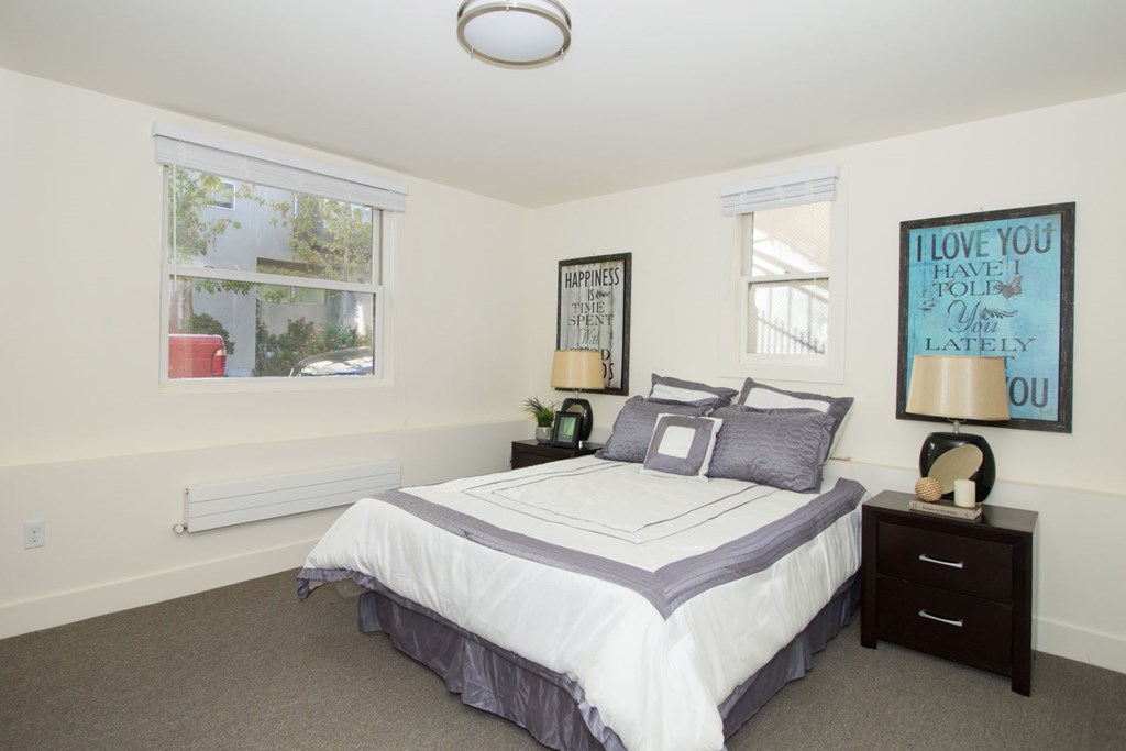 A bedroom with a bed, nightstand, and two framed pictures on the wall.