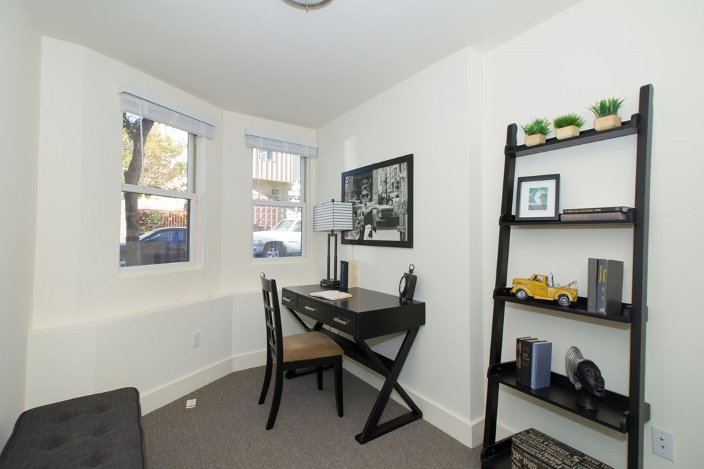 A black and white photo is hanging on the wall above a black desk with a chair.