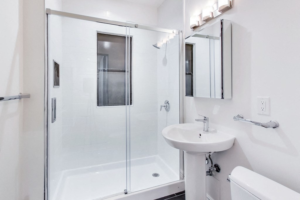 A white sink is in a white bathroom with a glass shower door.