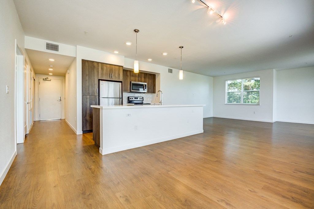 an empty kitchen and living room with wood floors and a white counter top