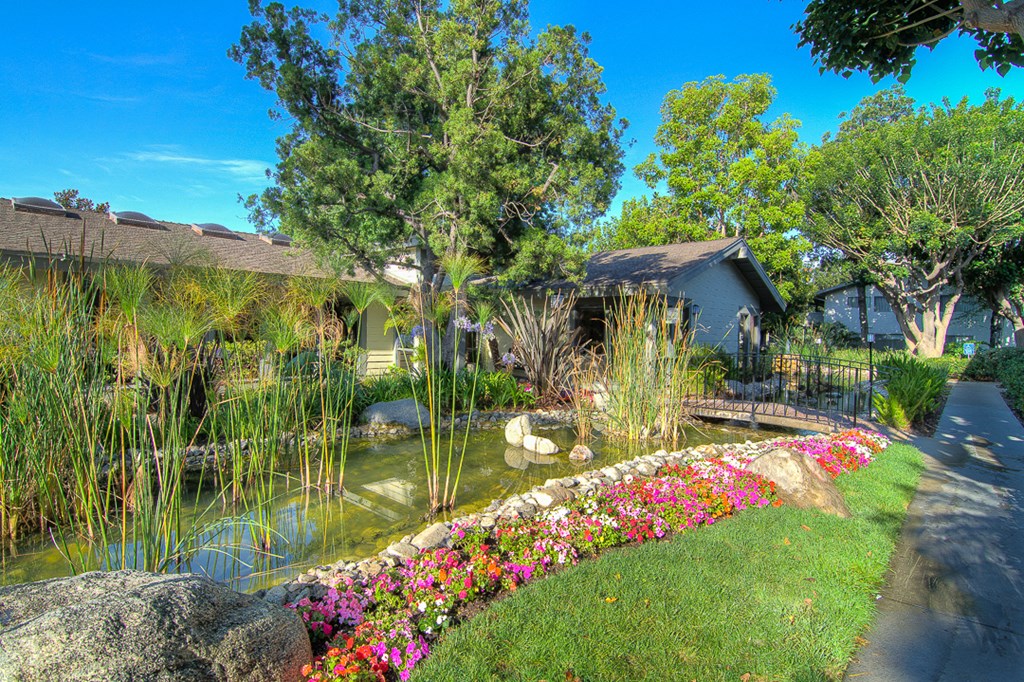a garden with a pond and flowers in front of a house