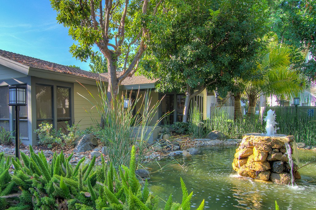 a fountain in the middle of a pond in front of a house