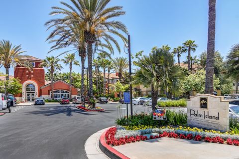 a parking lot with palm trees and flowers in front of a building