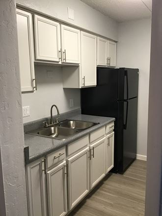 an empty kitchen with white cabinets and a black refrigerator