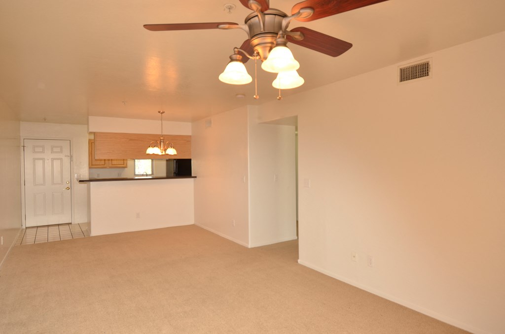 an empty living room with a ceiling fan and a kitchen