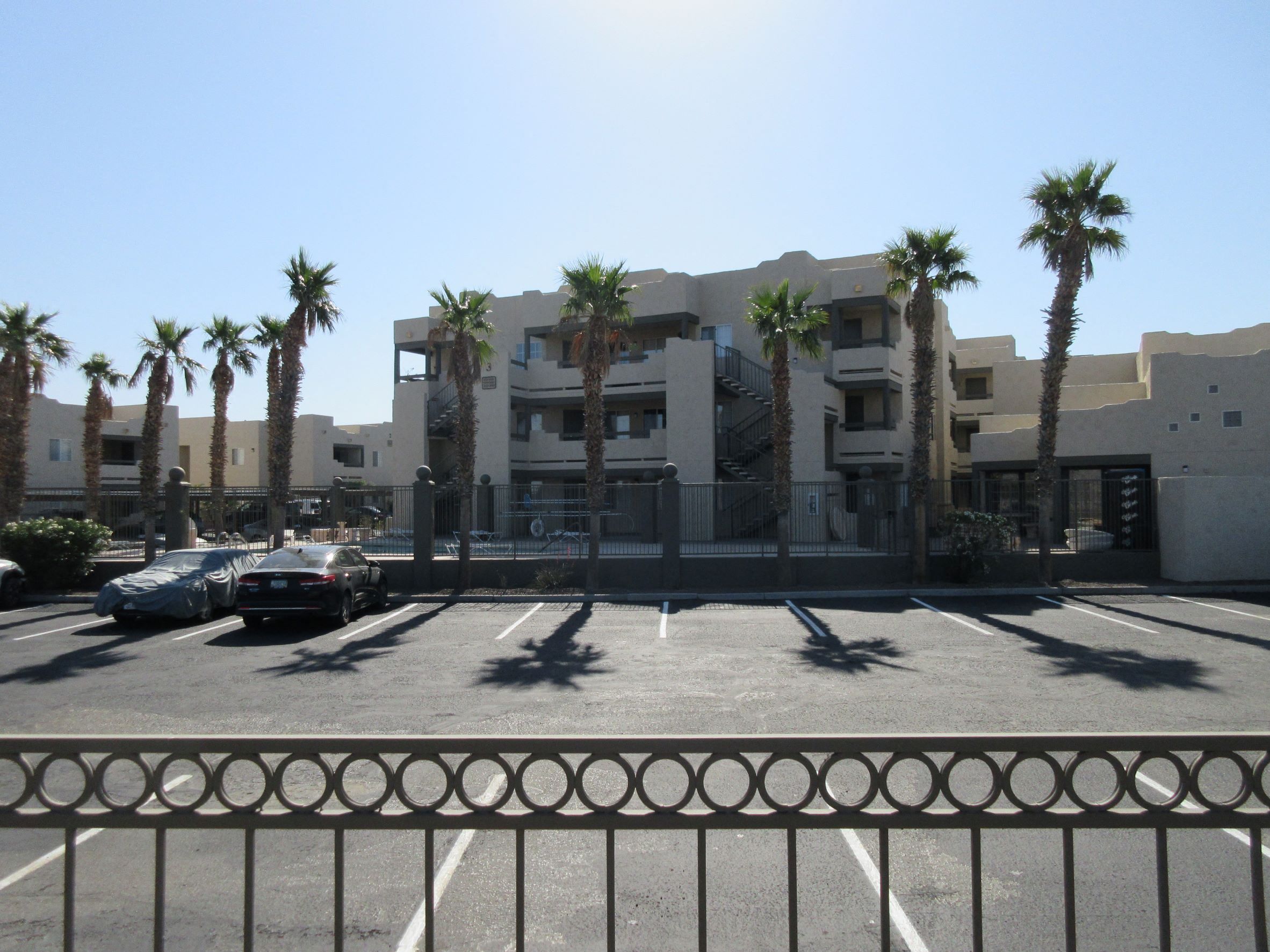 a parking lot in front of an apartment building with palm trees