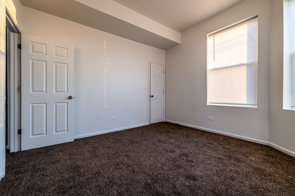 an empty bedroom with carpet and a door and window