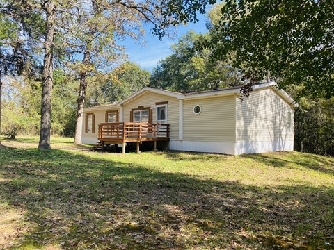 a small yellow house with a deck in the woods