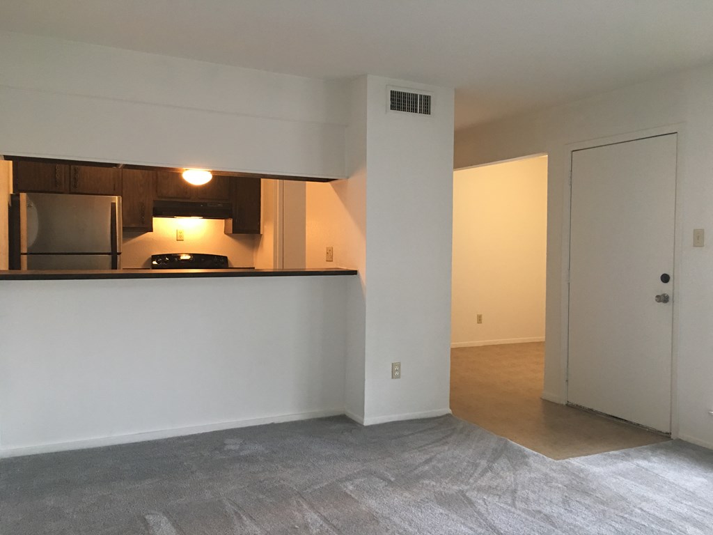 an empty living room with a kitchen and a door to a bedroom