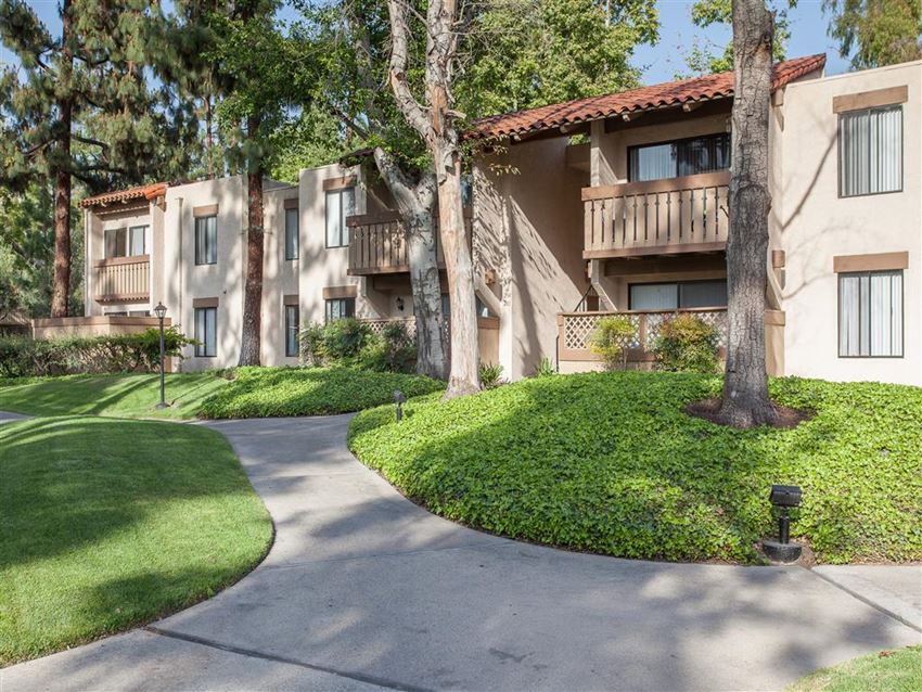 a walkway in front of an apartment building with trees and grass