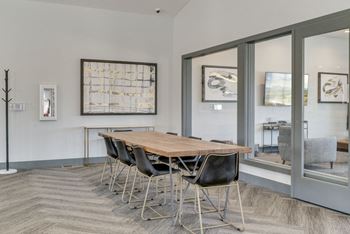 Long conference table in room enclosed with large glass windows looking out to great room