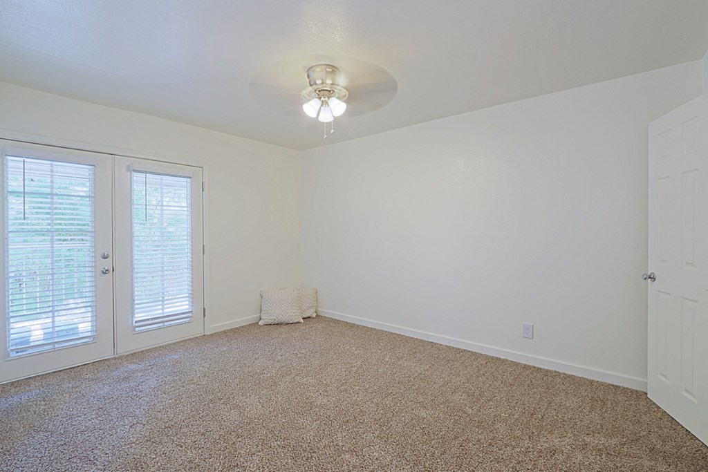 an empty living room with white walls and a white door and a ceiling fan