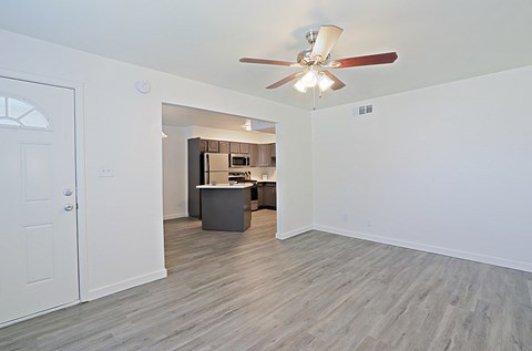 an empty living room with a ceiling fan and a kitchen