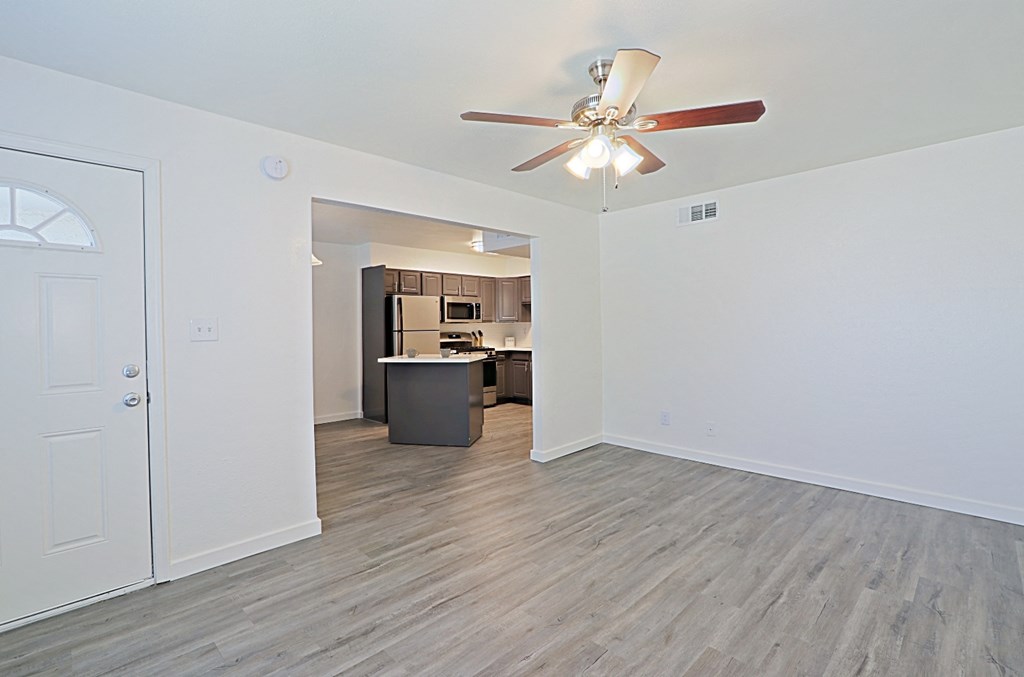 an empty living room with a ceiling fan and a kitchen