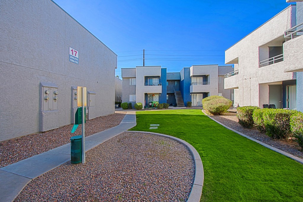 a pathway between two apartment buildings with a green lawn