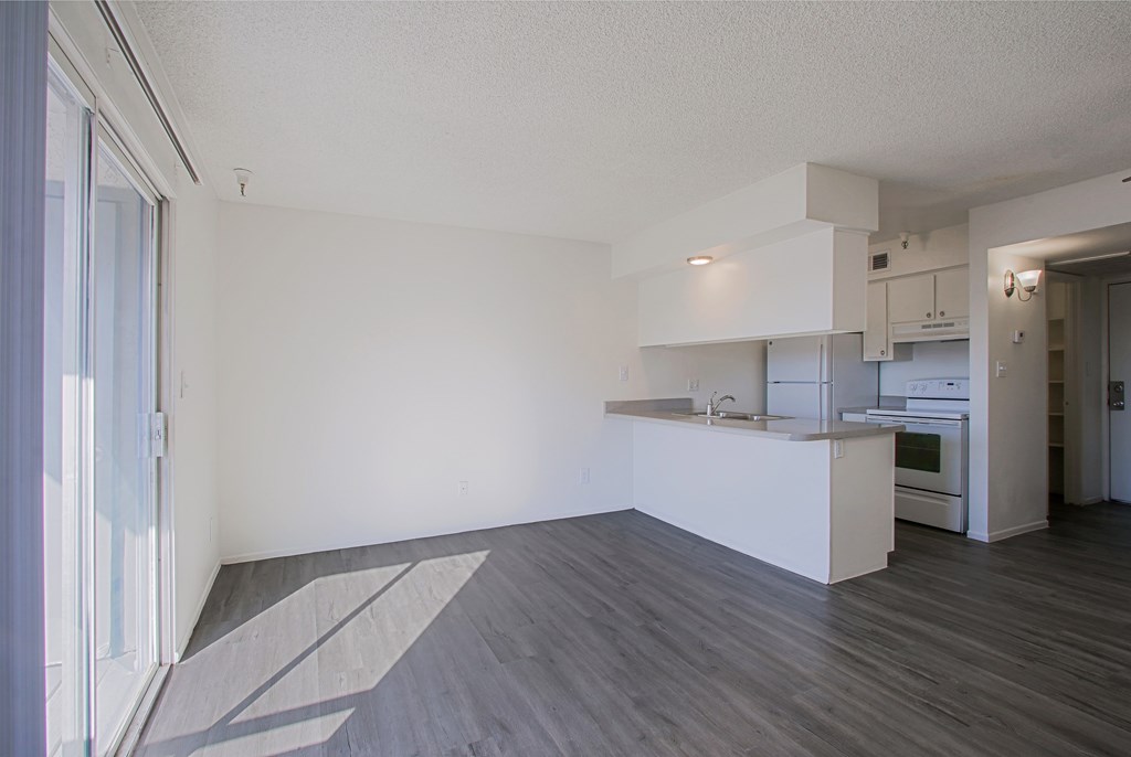 the living room and kitchen of an apartment with white walls and wood flooring