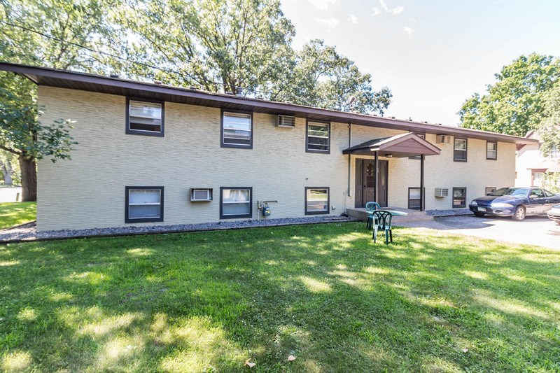the front of a white building with a green lawn and a car parked in front