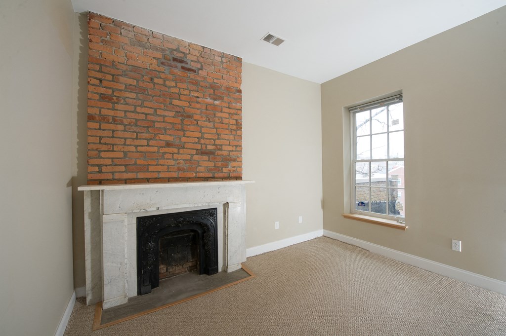 an empty living room with a brick fireplace and a window