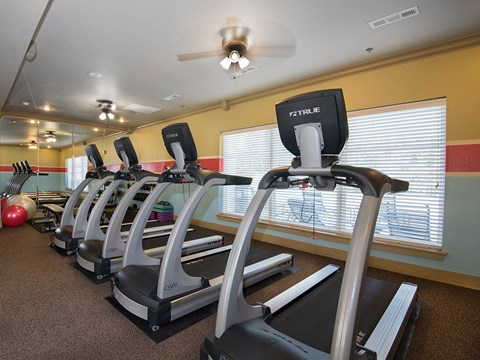 a gym with cardio machines and a ceiling fan