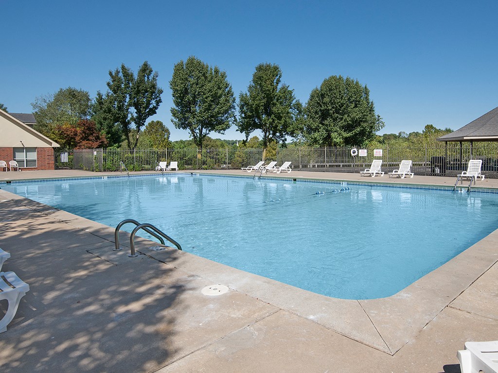 a swimming pool with chairs and trees in the background