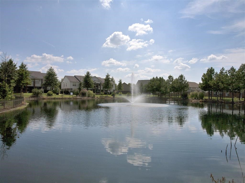 a fountain in the middle of a lake with houses in the background