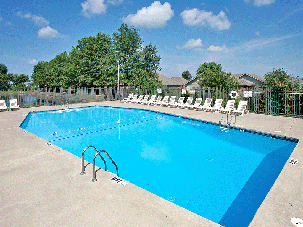 a swimming pool with white chairs around it and trees in the background