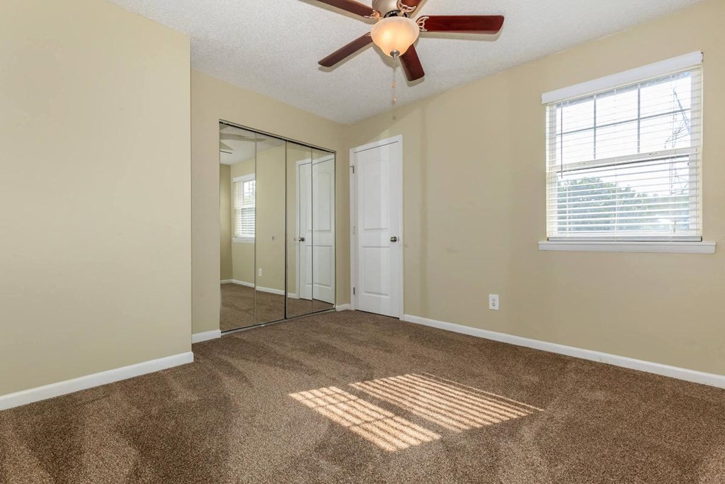 an empty living room with a ceiling fan and a mirror