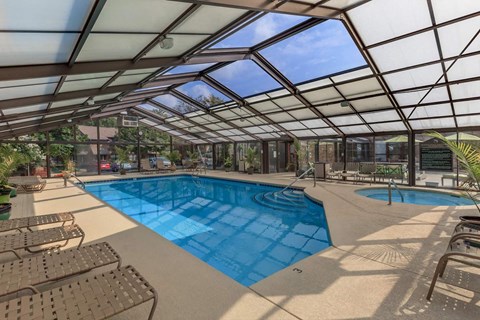 the pool is under a glass roof with chairs around it