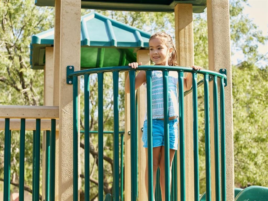a little girl standing at the gate of a playground