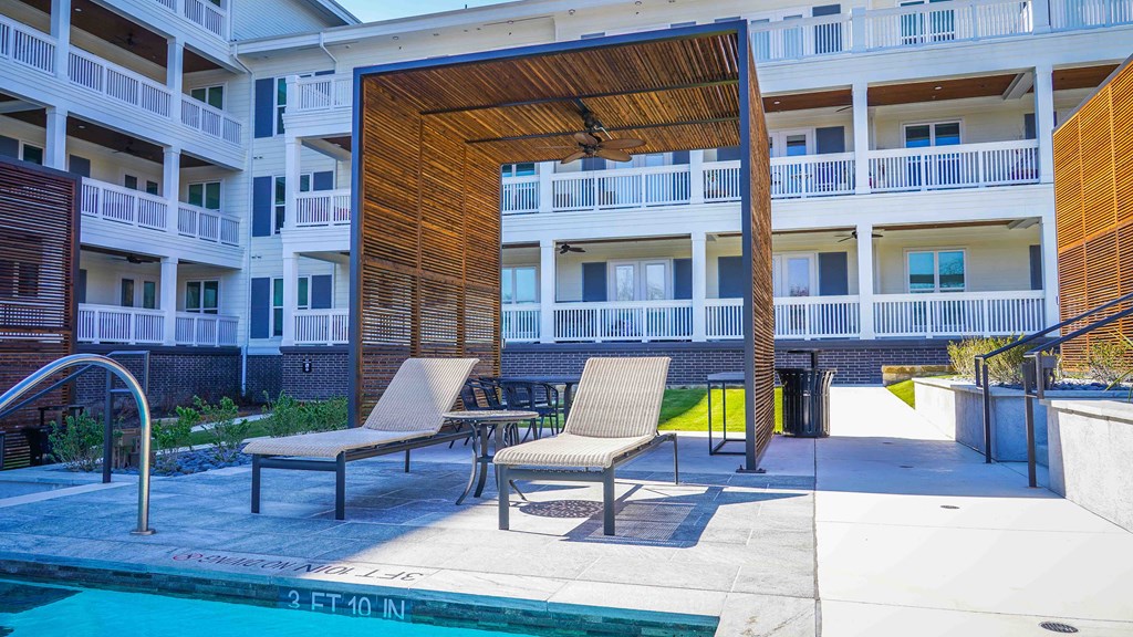 a patio with chairs and a pool in front of an apartment building