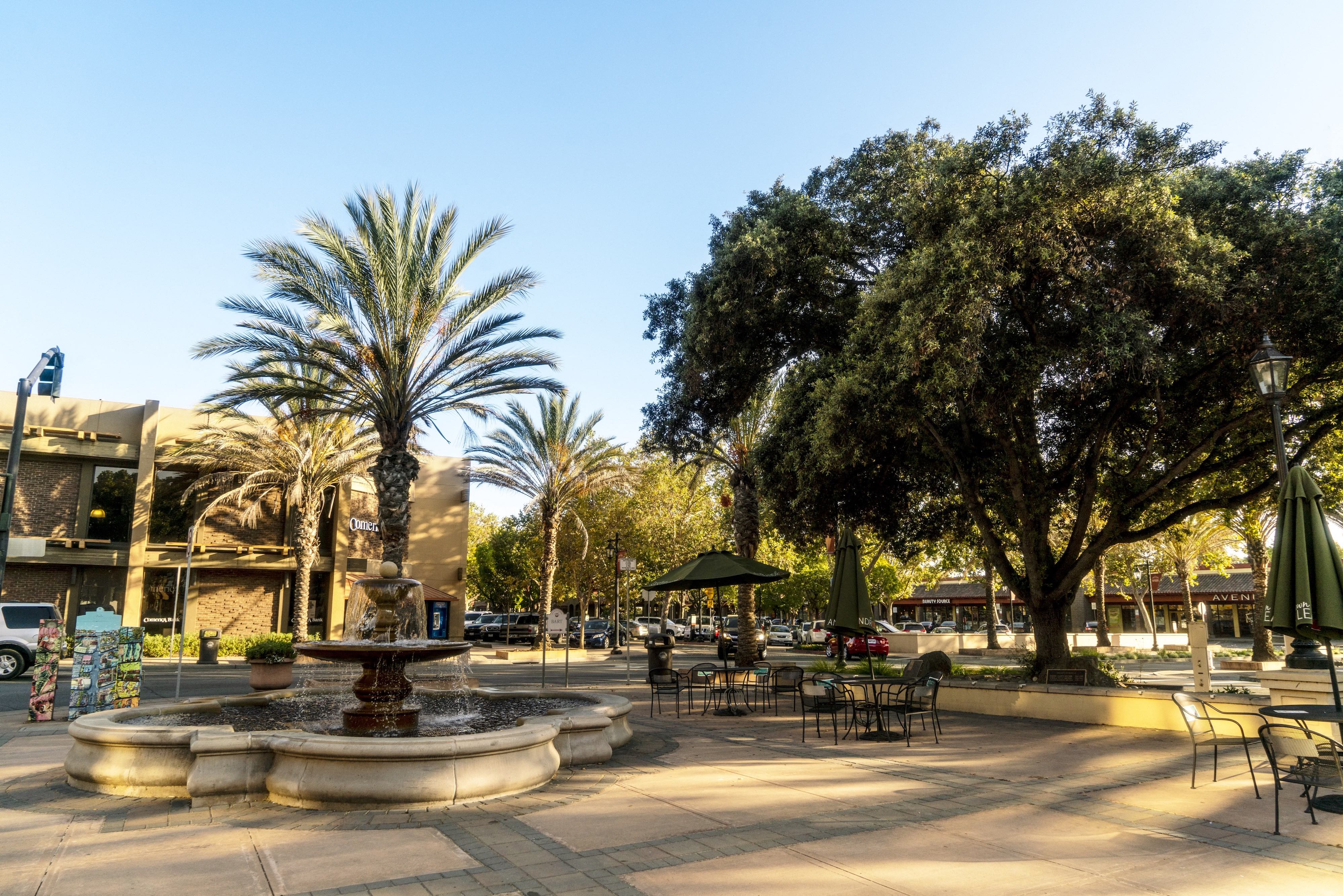 a fountain in the middle of a park with tables and chairs