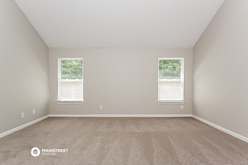 an empty room with two windows and carpeting