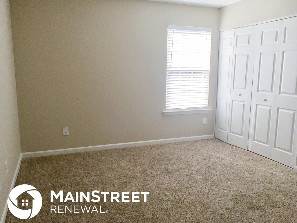 a room with a carpeted floor and two white doors and a window