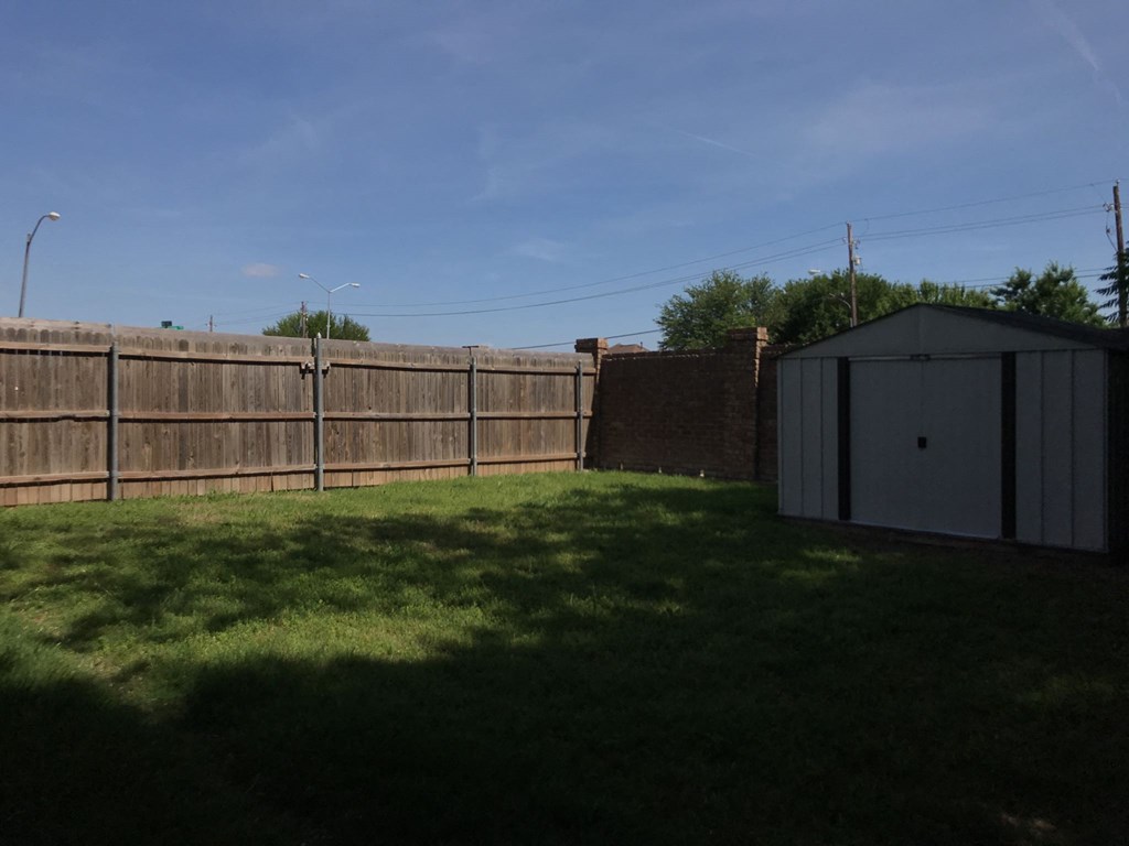 a backyard with a wooden fence and a shed and grass