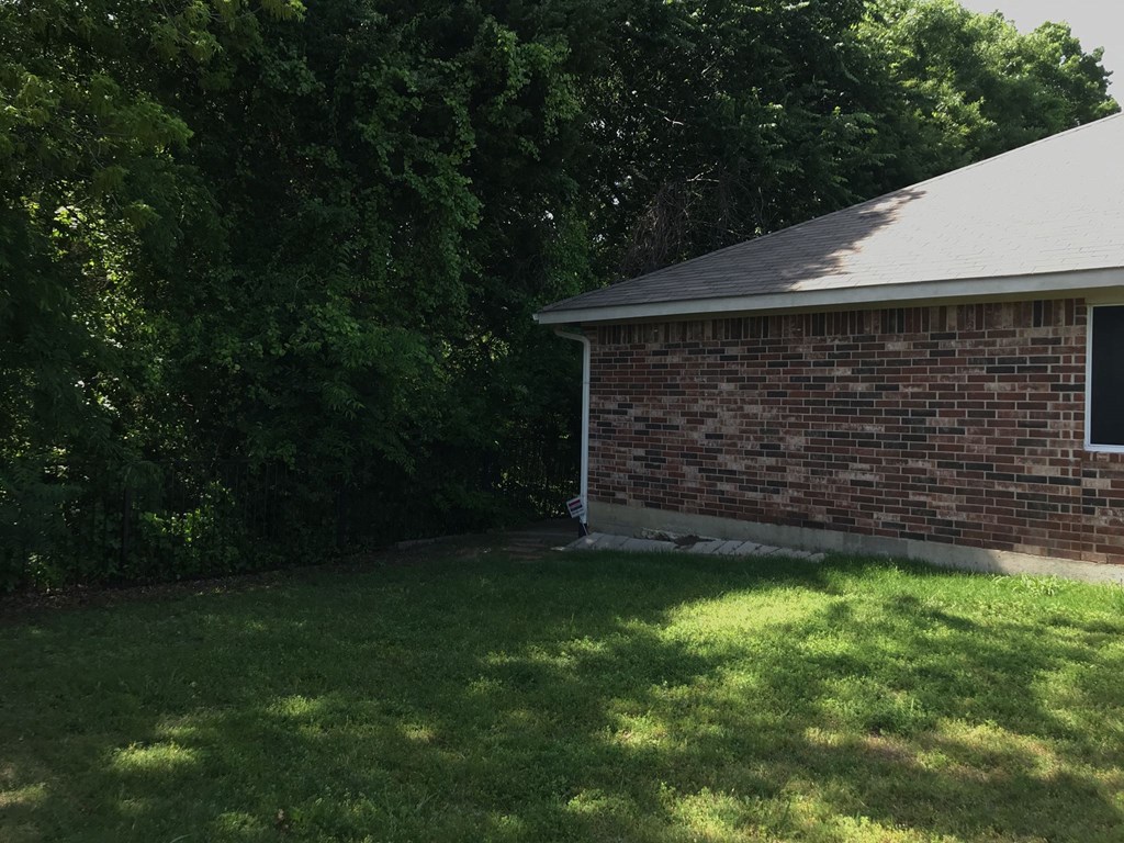 the back of a brick house with grass and trees