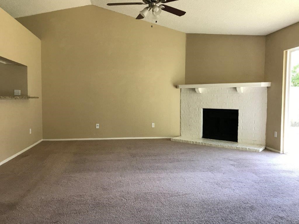 an empty living room with a fireplace and a ceiling fan