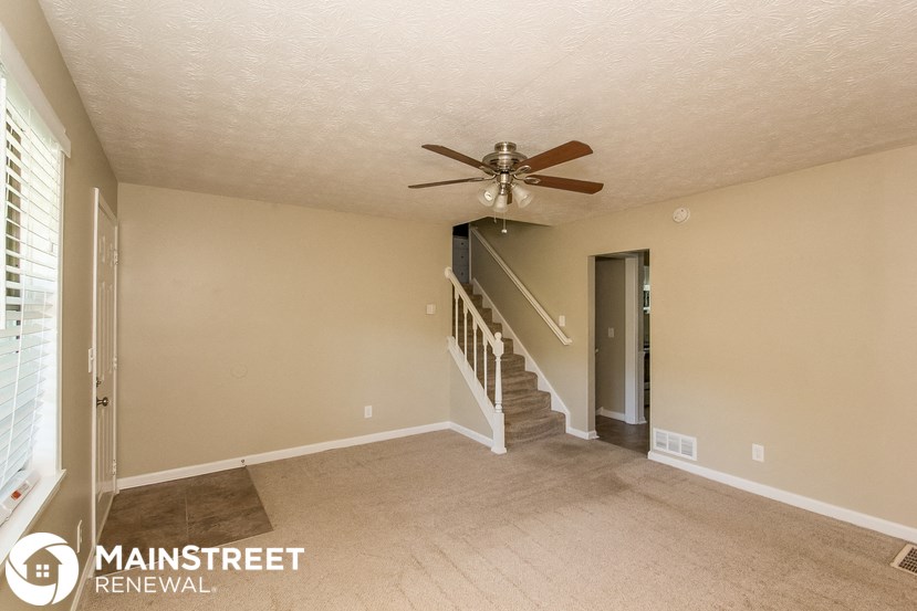 an empty living room with a ceiling fan and a staircase