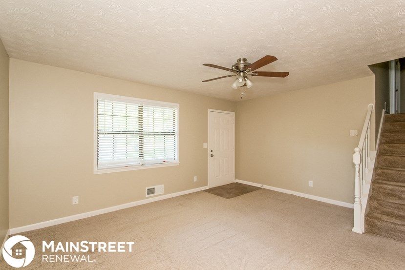 an empty living room with a ceiling fan and a staircase